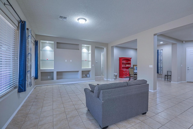 living room with a textured ceiling, baseboards, visible vents, built in shelves, and light tile patterned floors