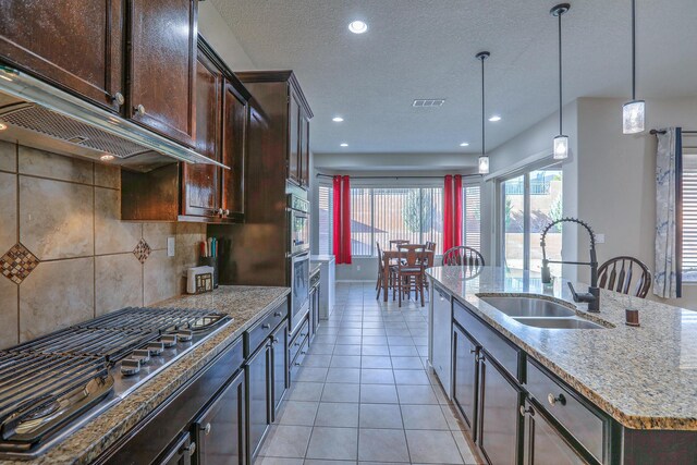 kitchen with light stone countertops, a sink, under cabinet range hood, stainless steel appliances, and visible vents