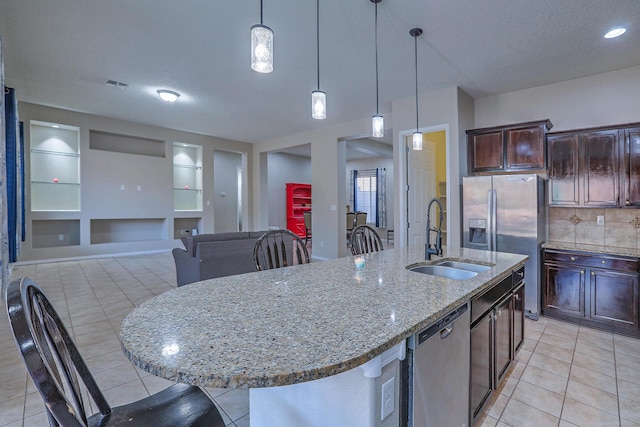 kitchen featuring stainless steel appliances, light tile patterned floors, a sink, a center island with sink, and built in shelves