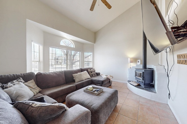 living room with high vaulted ceiling, a wood stove, light tile patterned floors, baseboards, and ceiling fan