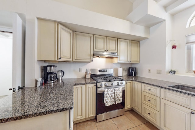 kitchen with cream cabinets, dark stone countertops, under cabinet range hood, and stainless steel range with gas cooktop