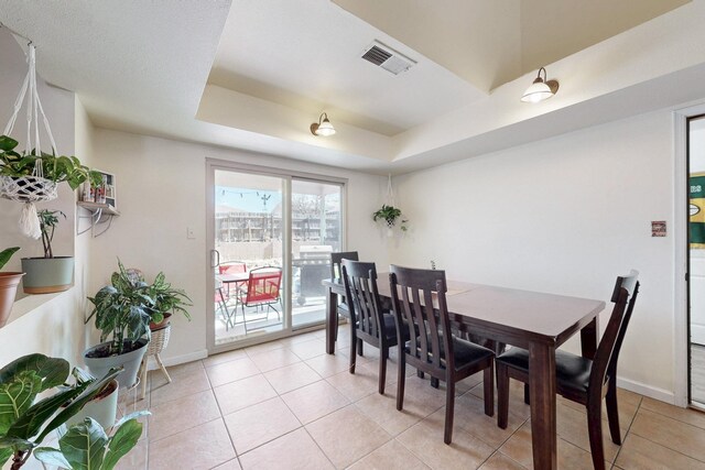 dining space with a tray ceiling, baseboards, visible vents, and light tile patterned floors