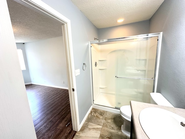 131 Las Ramblas Ave NW, Rio Rancho, NM 87144 - bathroom featuring a textured ceiling, toilet, a shower stall, baseboards, and wood finished floors