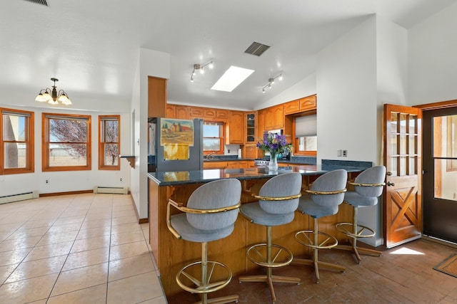 kitchen with brown cabinetry, lofted ceiling, glass insert cabinets, a baseboard radiator, and a notable chandelier