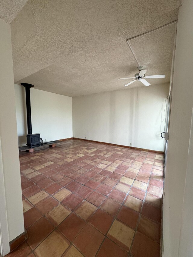 6488 Tahawash St, Cochiti Lake, NM 87083 - empty room with baseboards, a ceiling fan, a wood stove, and tile patterned flooring