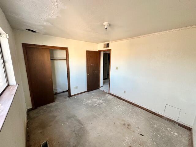 701 Houston Ave, Grants, NM 87020 - unfurnished bedroom featuring unfinished concrete floors, a closet, baseboards, and visible vents
