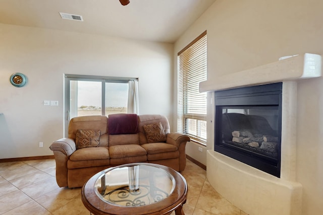living area featuring light tile patterned flooring, baseboards, visible vents, and a glass covered fireplace