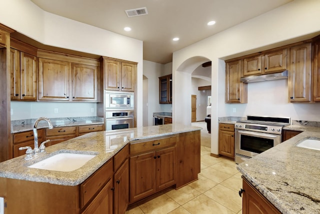 kitchen featuring visible vents, stainless steel appliances, arched walkways, under cabinet range hood, and a sink