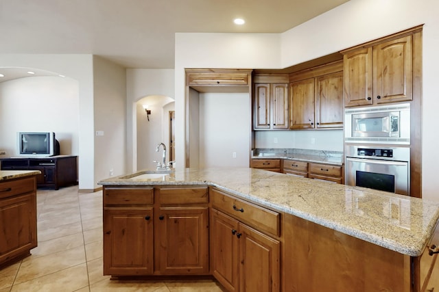 kitchen with light tile patterned floors, stainless steel appliances, a sink, arched walkways, and light stone counters