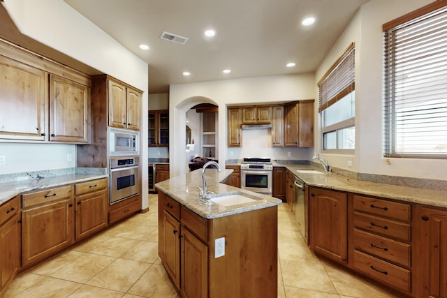 kitchen with stainless steel appliances, a sink, arched walkways, visible vents, and a kitchen island with sink