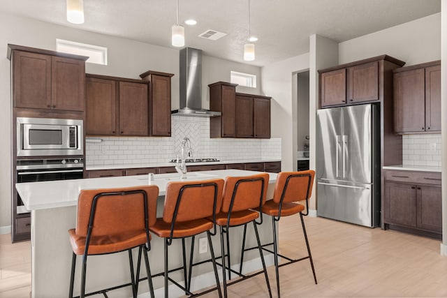 2422 Lynn Rd SE, Rio Rancho, NM 87124 - kitchen featuring an island with sink, wall chimney range hood, light countertops, appliances with stainless steel finishes, and backsplash