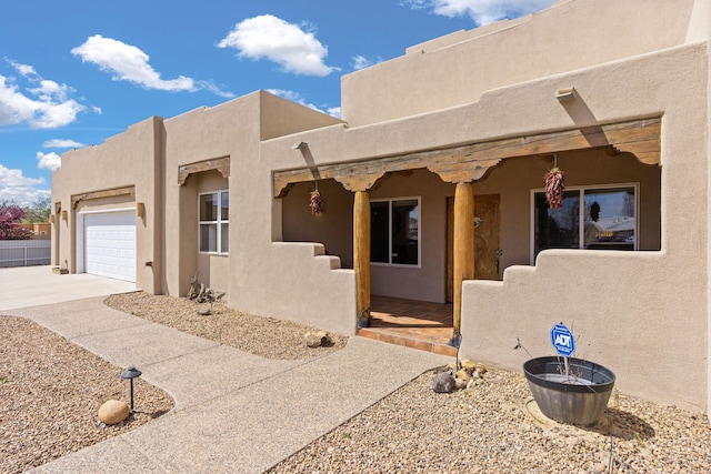 pueblo-style house with an attached garage, concrete driveway, and stucco siding