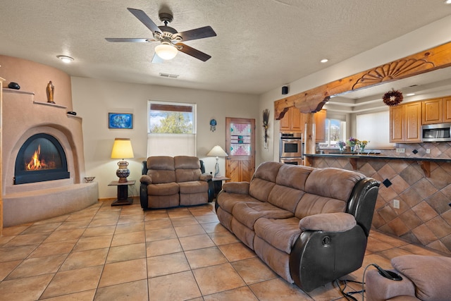 living area featuring visible vents, light tile patterned floors, ceiling fan, a textured ceiling, and a glass covered fireplace