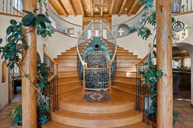 stairs featuring arched walkways, a towering ceiling, wood ceiling, tile patterned floors, and beam ceiling