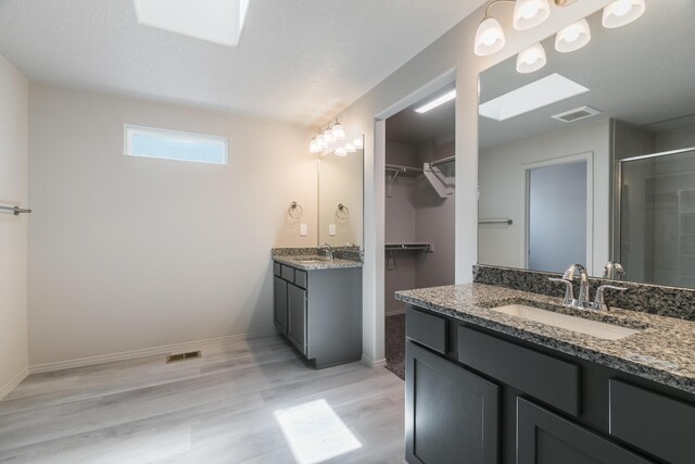 9600 Sage Ranch Ct SW, Albuquerque, NM 87121 - full bathroom with a stall shower, two vanities, wood finished floors, a walk in closet, and a skylight