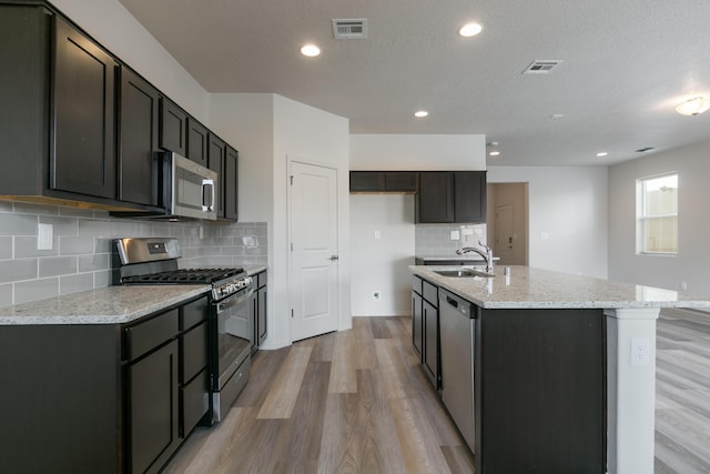 9504 Sage Ranch Ct SW, Albuquerque, NM 87121 - kitchen with appliances with stainless steel finishes, light wood-style flooring, light stone counters, backsplash, and a center island with sink
