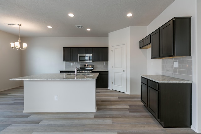 9504 Sage Ranch Ct SW, Albuquerque, NM 87121 - kitchen featuring appliances with stainless steel finishes, decorative backsplash, a textured ceiling, light stone countertops, and a chandelier