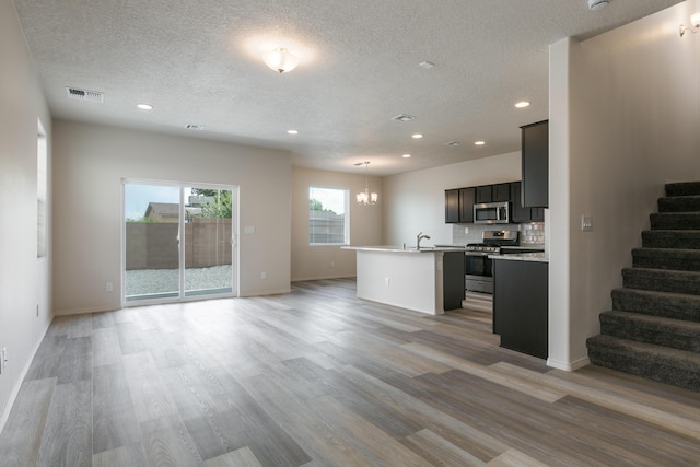 9504 Sage Ranch Ct SW, Albuquerque, NM 87121 - kitchen with appliances with stainless steel finishes, open floor plan, a chandelier, an island with sink, and light wood-style flooring