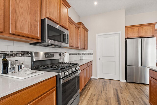 460 Rio Chama Cir SW, Los Lunas, NM 87031 - kitchen featuring stainless steel appliances, brown cabinetry, light wood-style floors, light countertops, and tasteful backsplash