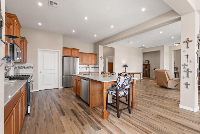 460 Rio Chama Cir SW, Los Lunas, NM 87031 - kitchen with appliances with stainless steel finishes, light wood finished floors, brown cabinets, open floor plan, and a kitchen breakfast bar