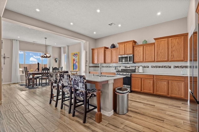 460 Rio Chama Cir SW, Los Lunas, NM 87031 - kitchen featuring appliances with stainless steel finishes, brown cabinets, light wood-type flooring, recessed lighting, and a textured ceiling