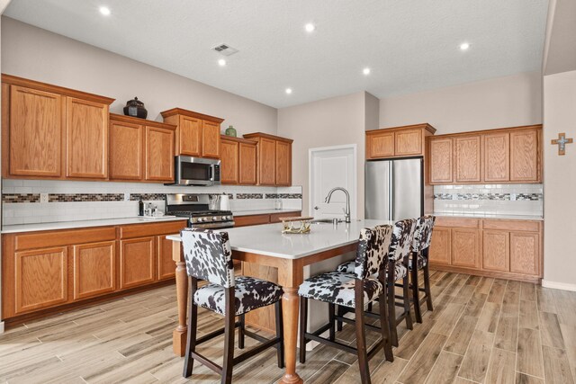 460 Rio Chama Cir SW, Los Lunas, NM 87031 - kitchen with stainless steel appliances, a breakfast bar, decorative backsplash, a sink, and light wood-style flooring