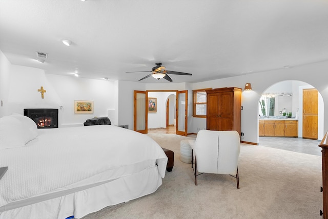 1125 Marigold Dr NE, Albuquerque, NM 87122 - bedroom featuring visible vents, a lit fireplace, arched walkways, light carpet, and a ceiling fan