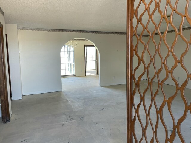 hall with unfinished concrete flooring, arched walkways, and a textured ceiling