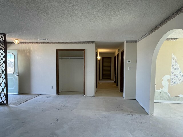 unfurnished bedroom with arched walkways, a textured ceiling, and unfinished concrete floors