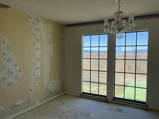spare room featuring an inviting chandelier, a textured ceiling, a healthy amount of sunlight, and visible vents
