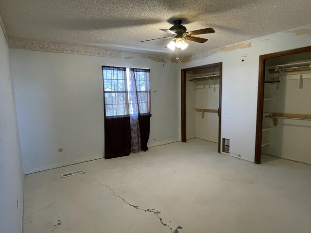 unfurnished bedroom with a textured ceiling, visible vents, a ceiling fan, and two closets