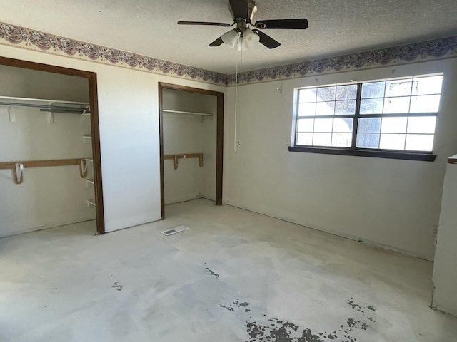 unfurnished bedroom with concrete floors, a textured ceiling, a ceiling fan, and two closets