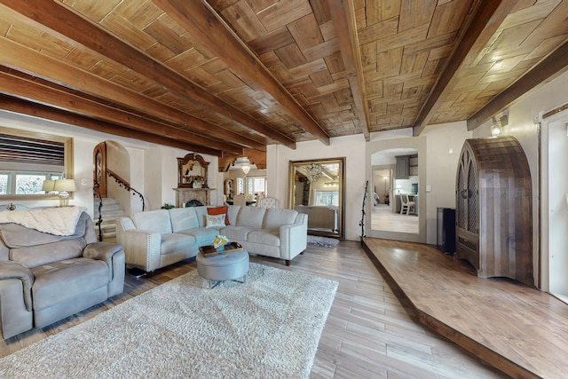 living area featuring wood finished floors, arched walkways, beamed ceiling, a fireplace, and wooden ceiling