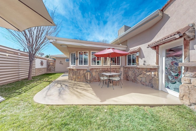 back of property featuring fence, a yard, stucco siding, a patio area, and stone siding