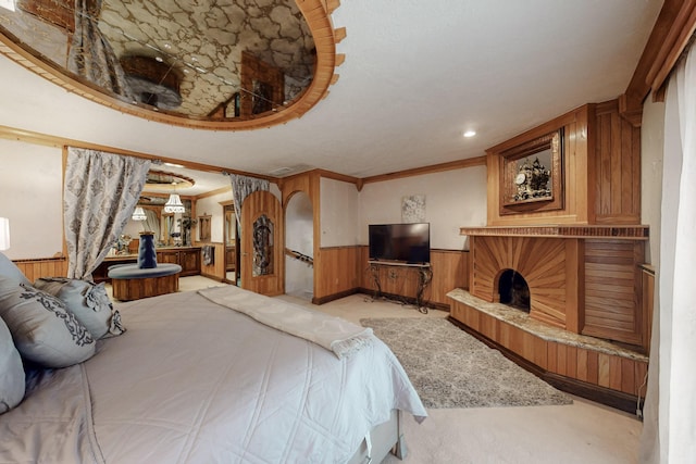 bedroom featuring a fireplace with raised hearth, wood walls, light colored carpet, and a wainscoted wall
