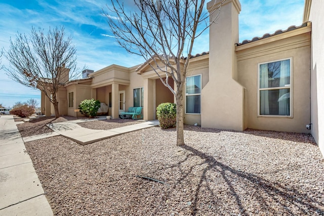exterior space with stucco siding, a chimney, and a tiled roof