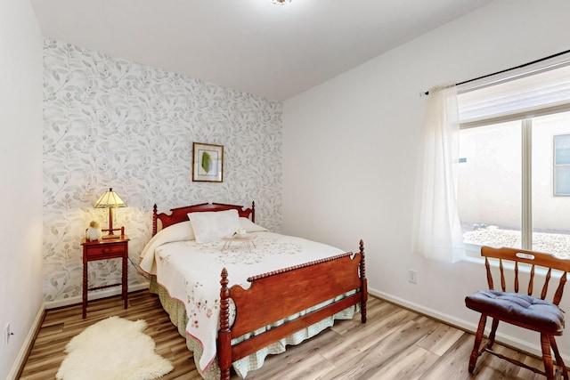 bedroom featuring baseboards, wallpapered walls, and light wood-style floors