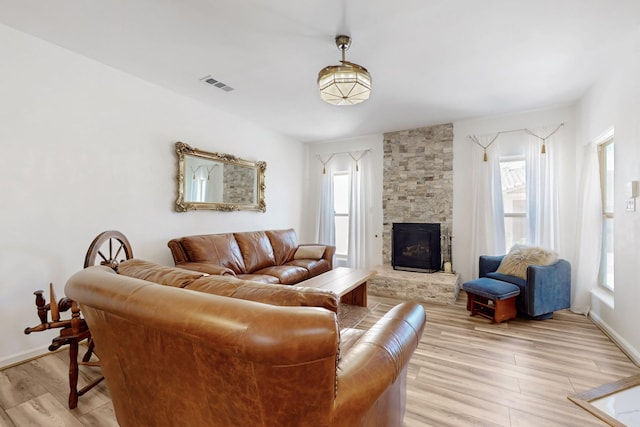 living room featuring a stone fireplace, baseboards, visible vents, and light wood-style floors
