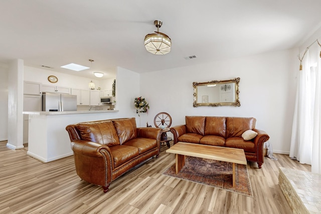 living area featuring light wood-type flooring, a skylight, baseboards, and visible vents