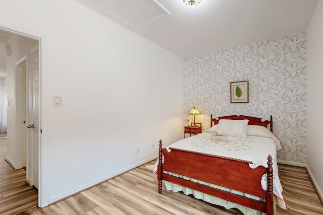bedroom featuring attic access, baseboards, wallpapered walls, and light wood-style floors
