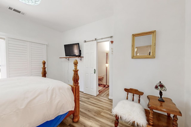 bedroom with visible vents, a barn door, light wood-style floors, and a closet