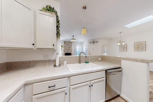 kitchen with white cabinets, a skylight, dishwasher, a sink, and decorative light fixtures