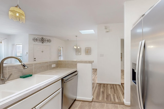 kitchen featuring light countertops, hanging light fixtures, a sink, a skylight, and appliances with stainless steel finishes