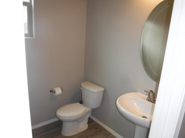 half bathroom with wood finished floors, toilet, baseboards, and a sink
