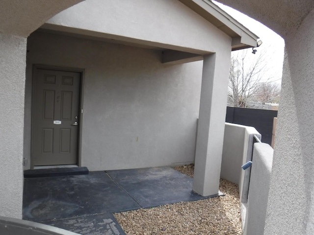 doorway to property with stucco siding and fence