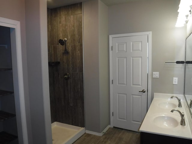 bathroom featuring wood finished floors, a sink, double vanity, and a tile shower