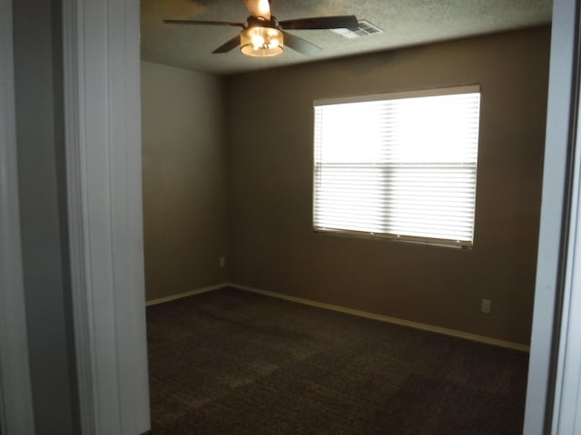 spare room featuring dark carpet, visible vents, baseboards, and ceiling fan