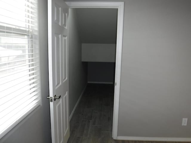 corridor with vaulted ceiling, baseboards, and dark wood-style flooring