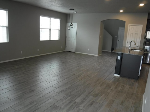 kitchen with light stone counters, a sink, arched walkways, dark wood finished floors, and recessed lighting