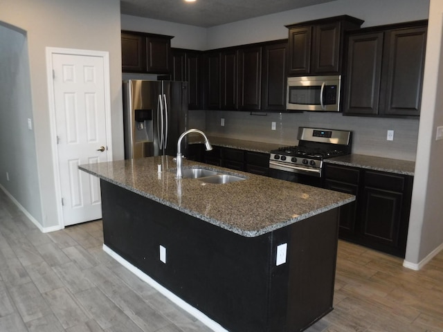 kitchen featuring stone countertops, a sink, baseboards, tasteful backsplash, and appliances with stainless steel finishes